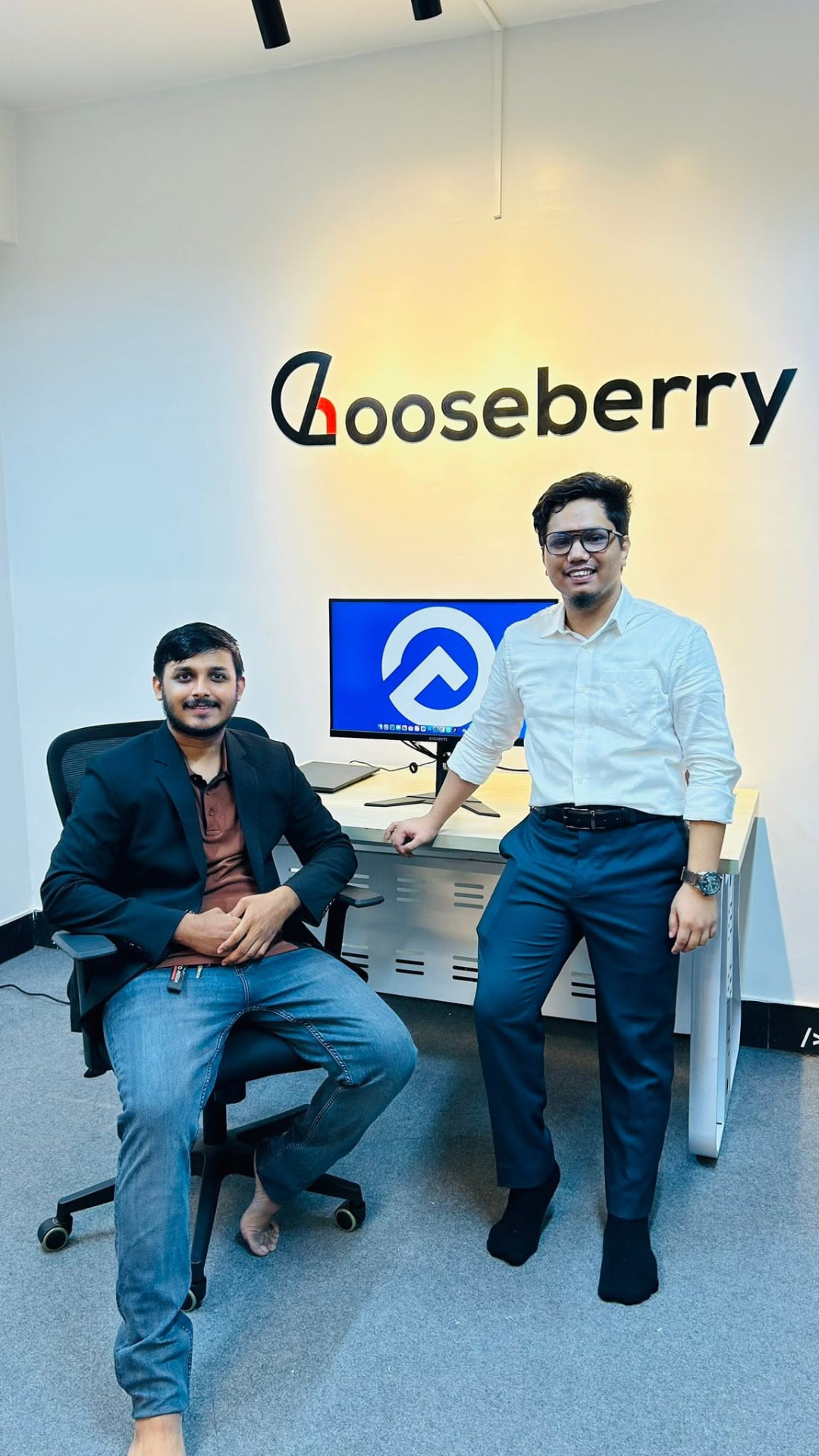 Gooseberry founders in front of the office logo wall